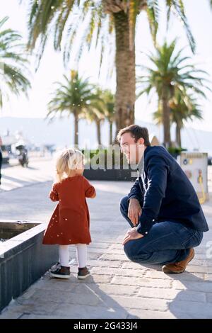 Das kleine Mädchen ist während ihres Vaters im Gesicht spritzeres Wasser Wandern auf einer Promenade Stockfoto