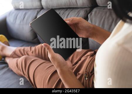 Gemischtes Geschlecht fließender Mann, der sich zu Hause auf der Couch mit Tablet-PC mit Kopierbildschirm entspannt Stockfoto