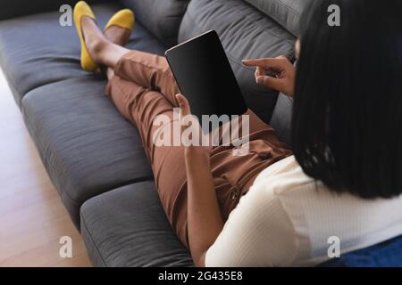 Gemischtes Geschlecht fließender Mann, der sich zu Hause auf der Couch mit Tablet-PC mit Kopierbildschirm entspannt Stockfoto