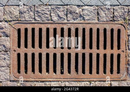 Rostiges Mannloch rechteckiges Gitter des Entwässerungssystems des Fußgängerwegs aus rauh geschnittenen Steinfliesen Draufsicht. Stockfoto
