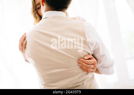 Die Braut umarmt den Bräutigam fest, der Bräutigam küsst sie, der Blick von der Rückseite des Bräutigams