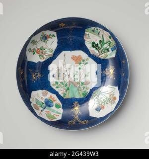 Untertasse mit Puderblau und Paneelen in Reserve mit Blütensprays, Landschaften und wertvollen Gegenständen. Schale mit runder Porzellanwand, in Unterglasur blau und auf der Glasur blau, rot, grün, gelb, Aubergine gemalt, Schwarz und Gold. Die Vorder- und Rückseite der Schale sind mit bleu poudré (puderblau) mit fünf in diese eingelassenen, geflammten Kartuschen bedeckt; auf der Ebene ein Stein mit Rohrzweigen; An der Wand ein prunus-Zweig, eine Flusslandschaft, ein Blumenzweig und Antiquitäten und Wertgegenstände (Vase, Artemisia-Blatt), mit einer Blume in Gold auf dem Blau dazwischen; der Rücken mit abgenutzten Blumenzweigen in GO Stockfoto