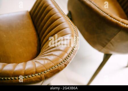 Eine Nahaufnahme der Rückseite des Stuhls, die sich in eine Armlehne aus braunem echtem Leder verwandelt. Stockfoto