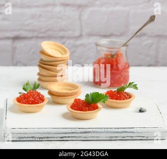 Roter Kaviar im Glasgefäß und runde Törtchen auf einem weißen Tisch Stockfoto