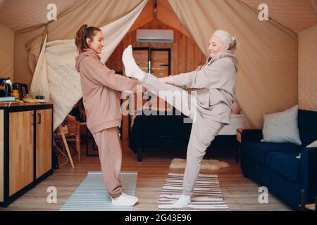 Familie macht Aufwärmen Übungen Sport drinnen. Junge und ältere Frauen entspannen sich im Glamping-Zelt. Mutter und d Stockfoto