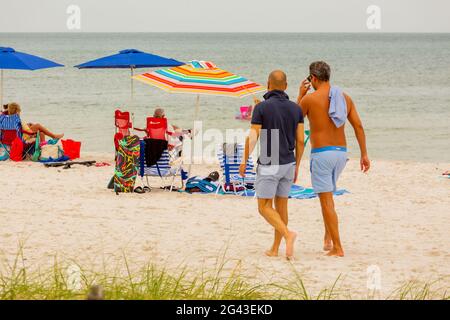 Zwei Männer, die in Florida mit Sonnenschirmen und dem Golf von Mexiko im Hintergrund den Strand entlang laufen Stockfoto