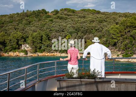 Paar auf Geländer des Kreuzfahrtschiffes mit Küste dahinter, in der Nähe von Kampor, Primorje-Gorski Kotar, Kroatien, Europa Stockfoto