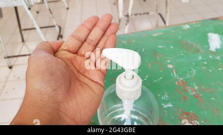 Die Hand eines Mannes hat Alkohol-Gel in der Hand, daneben wird eine Flasche Alkohol-Gel platziert. Die Lehrer waschen sich die Hände mit Alkoholgel, bevor sie in den eintreten Stockfoto