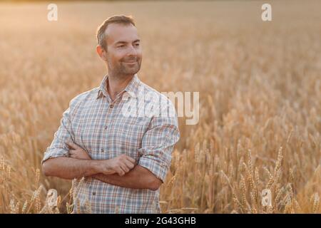 Mann Bauer im Weizenfeld bei Sonnenuntergang. Landwirtschaft und landwirtschaftliche Ernte, Stockfoto