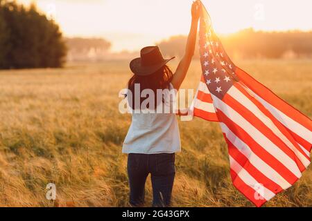 Frau Bäuerin auf dem landwirtschaftlichen Feld mit amerikanischer Flagge auf Sonnenuntergang Stockfoto