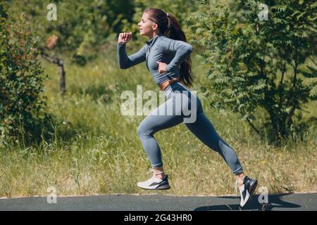 Laufendes Mädchen im Stadtpark. Junge Frau Läuferin beim Joggen im Freien. Seitenansicht. Stockfoto