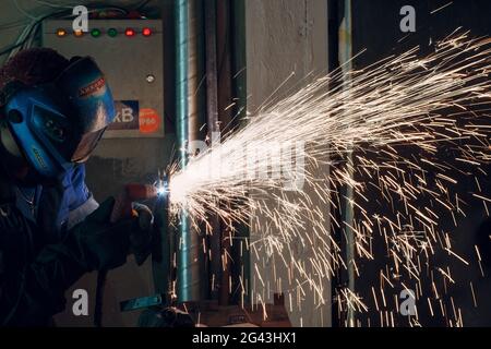 Mann in Maske schneidet Metall mit Plasmaschneider. Helm und Spakren Stockfoto