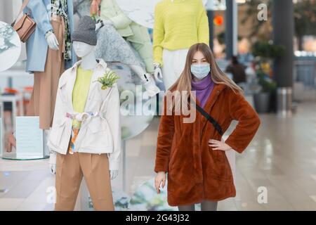 Junge asiatische Frau in einer medizinischen Maske neben Schaufensterpuppen in einem Geschäft. Stockfoto