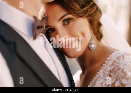 Nahaufnahme einer Braut, die die Kamera ansah, ihren Kopf auf die Brust des Bräutigams legte. Wunderschönes Hochzeitspaar. Fine-Art Weddi Stockfoto