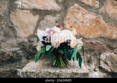 Brautstrauß aus weißen und rosa Pfingstrosen, Rosen, Ästen von Eukalyptusbäumen, Calla-Lilien und dekorativer Artischocke auf dem Stein Stockfoto