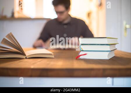 Konzept lernen und studieren. Stapel von Büchern im Vordergrund, junger männlicher Student in verschwommenem Hintergrund Stockfoto