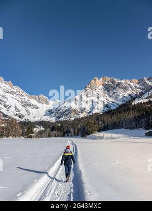 Sonnige Winterlandschaft in der Natur: Mädchen geht auf verschneiten Fußwegen, Bergkette, verschneiten Bäumen, Sonnenschein und blauem Himmel Stockfoto