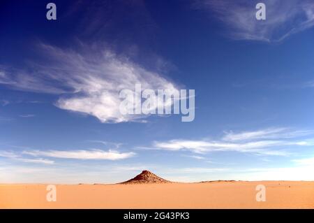 Ein Felsvorsprung aus Sandstein unter weißen Wolken tief in der Westlichen Wüstensahara, in der Nähe des Gilf Kebir, im Südwesten Ägyptens. Stockfoto