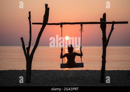 Silhouette einer jungen Frau auf Schaukel am Ong lang Beach bei Sonnenuntergang, Ong lang, Phu Quoc Island, Kien Giang, Vietnam, Asien Stockfoto