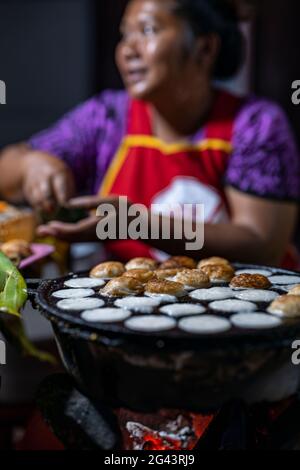 Köstliche Kokosnusspfannkuchen werden auf dem Nachtmarkt auf der Sisavangvong Road (Hauptstraße), Luang Prabang, Provinz Luang Prabang, Laos, über Holzkohle gebacken Stockfoto