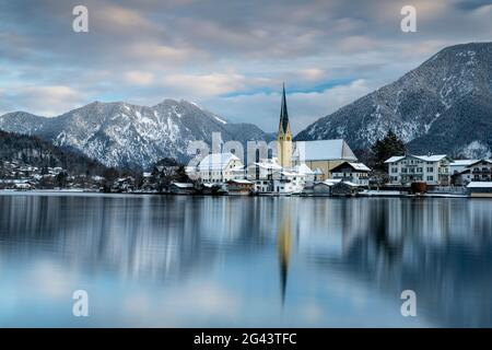 Blick über den winterlichen Tegernsee auf das Dorf Rottach-Egern mit der Kirche Sankt Laurentius, Bayern, Deutschland. Stockfoto