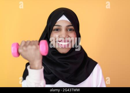 Die afro-muslimische Frau fördert ein gesundes Leben, indem sie Kurzhanteln in den Händen hält Stockfoto