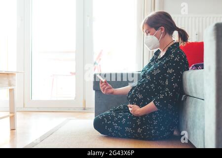 Quarantäne zu Hause. Eine Schwangere mit ffp2-Gesichtsmaske sitzt auf dem Boden und hält den Express-Antigencovid-Test Stockfoto