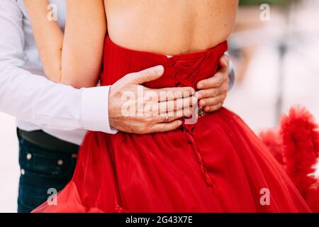 Die Hände des Mannes umarmen die Taille einer Frau in einem roten gekleidet Kleid Stockfoto