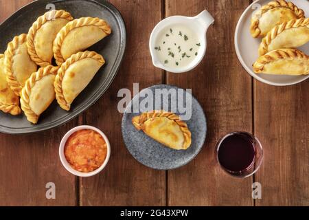 Empanadas mit Saucen und Wein, von oben auf dunklem Holzgrund geschossen Stockfoto