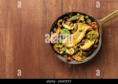 Nahaufnahme eines rustikalen Pilzes und Oliven, die mit Minze anbraten, von oben geschossen Stockfoto