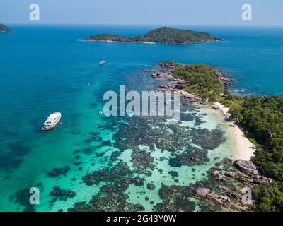 Luftaufnahme von John's Tours No. 9 Ausflugsboot und Touristen schnorcheln in klarem Wasser in der Nähe von Strand mit Kokospalmen, Dam Ngang Island, in der Nähe von Phu Quoc Stockfoto