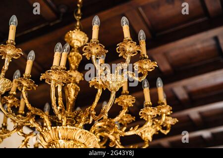 Elektrischer Kronleuchter mit Glühbirnen. Antiker goldener Kronleuchter im Inneren einer alten Villa. Stockfoto