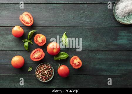 Bio-Tomaten aus Erbstück mit Basilikumblättern auf dunklem, rustikalem Hintergrund Stockfoto