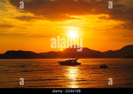 Weiße Motoryacht segelt auf dem Meer vor dem Hintergrund Von Bergen bei Sonnenuntergang Stockfoto