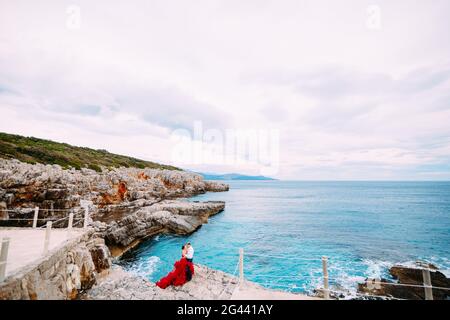 Ein Paar umarmt sich an einem Steinpier an einem felsigen Strand Stockfoto