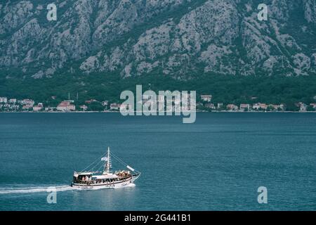 Weiße Segelyacht mit Touristen an Bord segelt entlang der Kotor Bucht vor der Kulisse der Berge und der alten Stadt Stockfoto