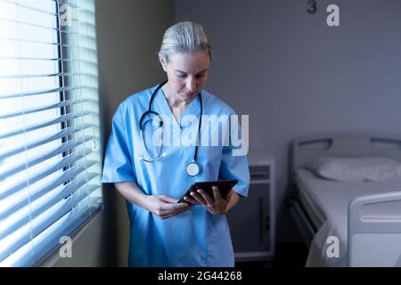Kaukasische Ärztin im Krankenhaus trägt Peelings und Stethoskop mit Tablet Stockfoto