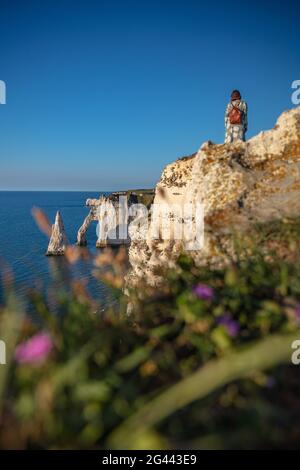 Eine Frau sitzt an der Alabasterküste und blickt auf den Felsenbogen Porte d&#39;Aval und die Felsennadel Aiuille in der Nähe von Étretat, Normandie, Frankreich. Stockfoto