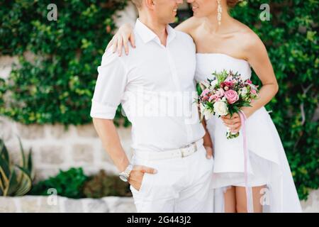 Die Braut und der Bräutigam stehen umarmt in einem schönen efeubedeckten weißen Haus in der Altstadt von Perast, aus nächster Nähe Stockfoto