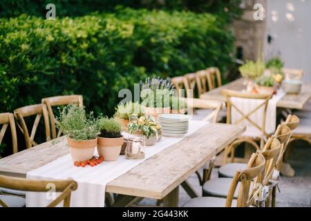 Empfang am Tisch für Hochzeitsessen bei Sonnenuntergang im Freien. Alte rechteckige Holztische mit Lappen Läufer, Holz Vintage Stühle, Lave Stockfoto