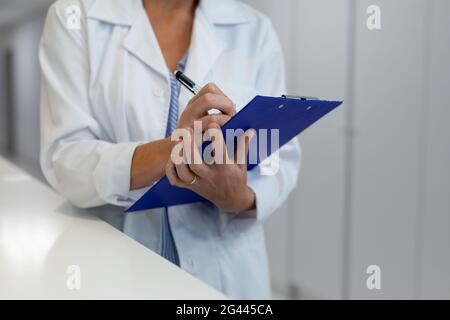 Mittelteil der kaukasischen Ärztin, die im Krankenhausflur steht und sich füllt Dokument mit medizinischen Diagrammen Stockfoto