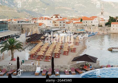 Blick auf den kleinen Strand der Altstadt von Budva, Montenegro vor der Kulisse der grünen Berge. Es gibt Sonnenliegen Stockfoto