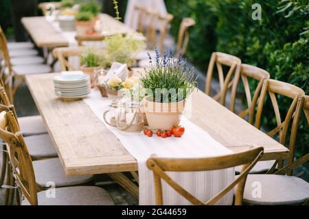 Empfang am Tisch für Hochzeitsessen bei Sonnenuntergang im Freien. Alte rechteckige Holztische mit Lappen Läufer, Holz Vintage Stühle, Lave Stockfoto