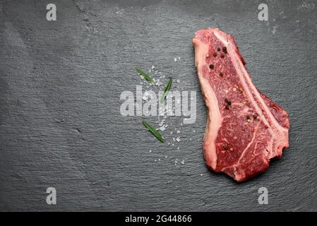 Frisches rohes Stück Rindfleisch, Striploin Steak liegt auf einem schwarzen Brett mit Gewürzen Stockfoto