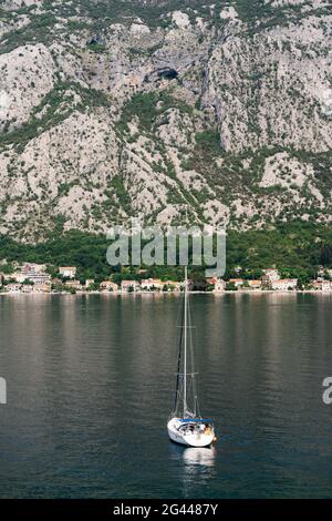 Weiße Segelyacht segelt entlang der Bucht von Kotor vor der Kulisse der Berge. Rückansicht Stockfoto