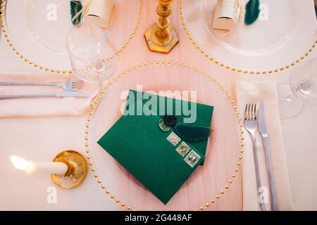 Leere grüne Umschläge mit Stempel liegen auf einer transparenten Platte auf einem Set-Tisch. Links brennt eine brennende Kerze. Draufsicht Stockfoto