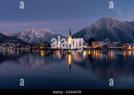 Blick über den winterlichen Tegernsee auf das Dorf Rottach-Egern mit der Kirche Sankt Laurentius, Bayern, Deutschland. Stockfoto