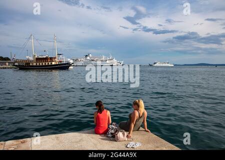 Zwei junge Frauen entspannen sich entlang der Strandpromenade mit Schiffen im Hafen, Split, Split-Dalmatien, Kroatien, Europa Stockfoto