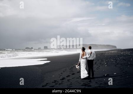 Reiseziel Island Hochzeit. Ein Hochzeitspaar läuft am schwarzen Strand von Vic entlang. Sandstrand mit schwarzem Sand am Ufer Stockfoto