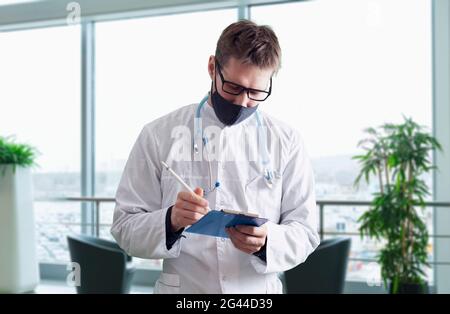 Junge männliche Arzt in Uniform trägt die Schutzmaske im Krankenhaus, medizinische Klinik Stockfoto